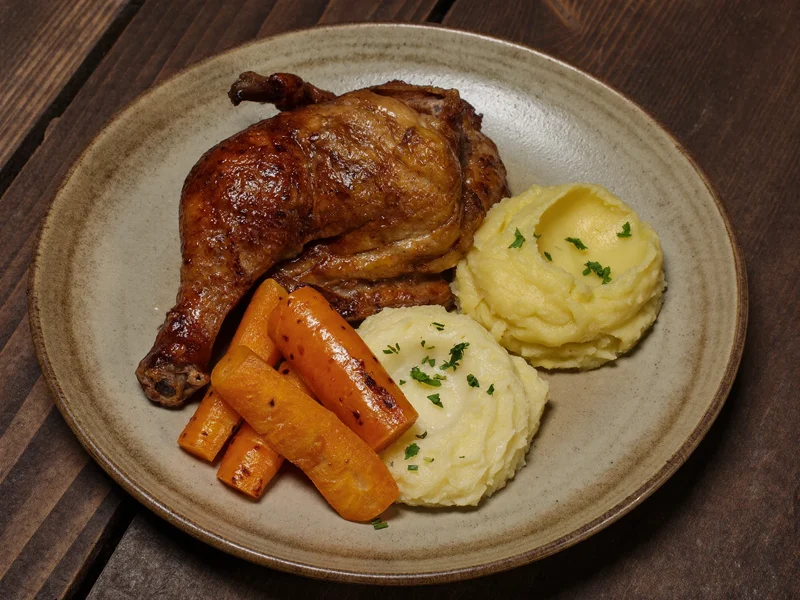 Zartes Schmorhuhn mit glattem Kartoffelpüree und gedämpften Karotten auf Steingutteller